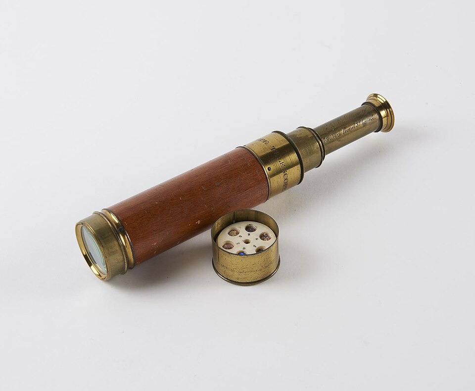 An antique telescope in brass and wood with its cap lying beside it